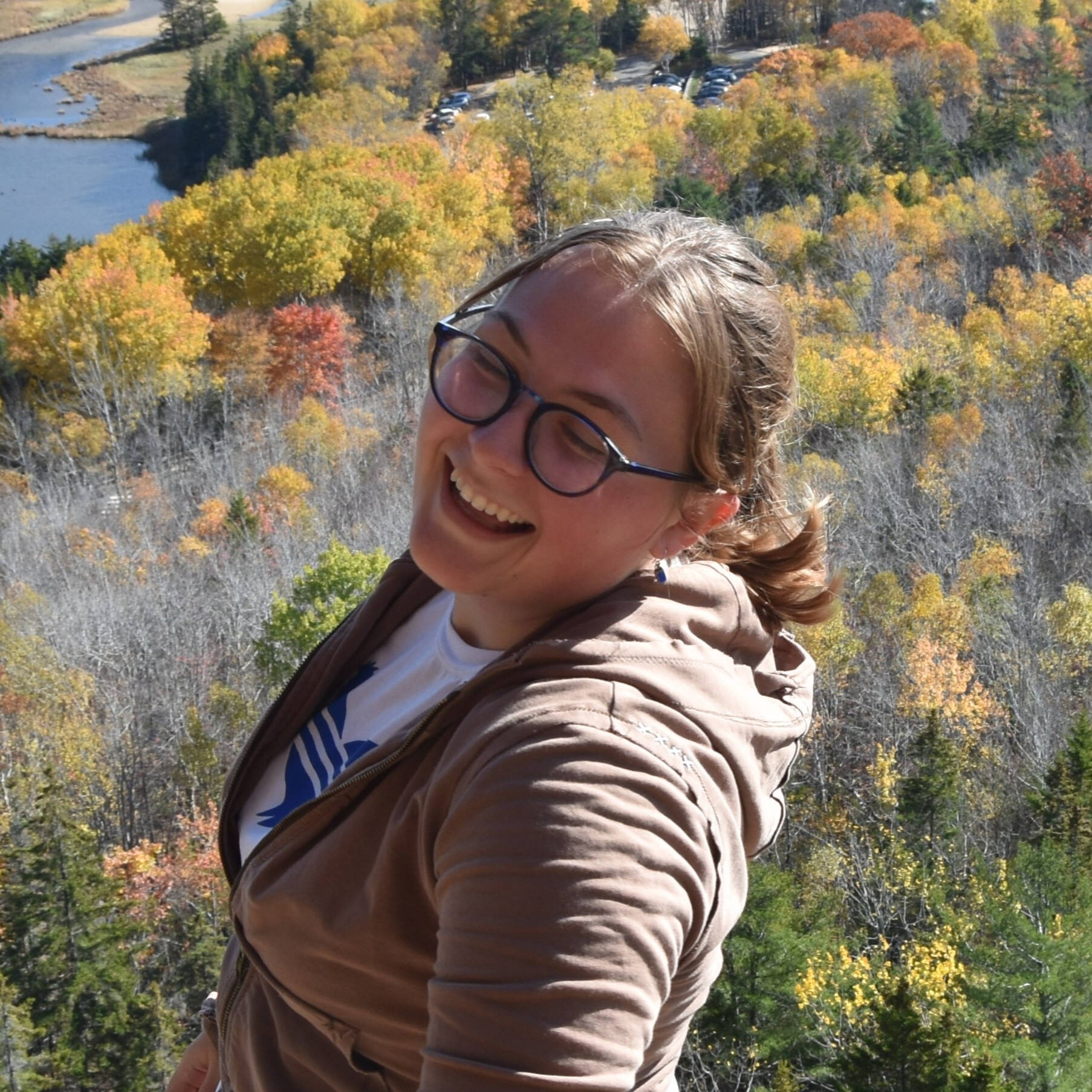 Emma Campbell poses for a photo on a hilltop with a river and forest in the background.